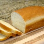 A loaf of white bread with a few slices cut from it on a wooden cutting board